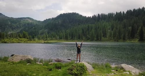 Aerial image of a lake and a beautiful woman while hiking, arrives at the destination after walkin