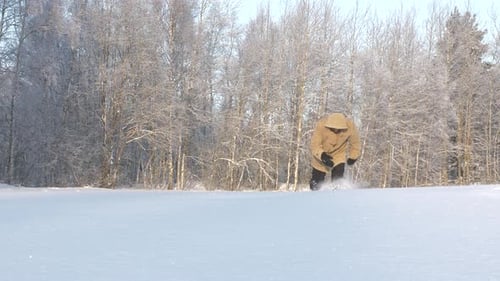 Mann geht durch Tiefschnee im Wald auf die Kamera zu und an ihr vorbei