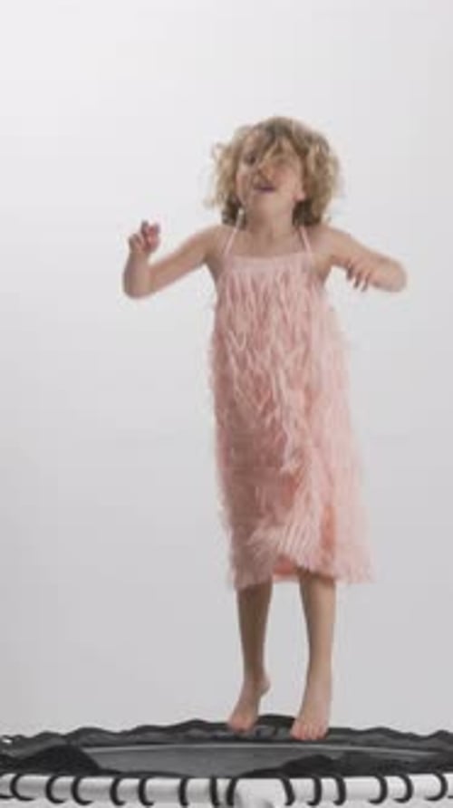 Girl Bouncing on Trampoline Wearing Pink Dress