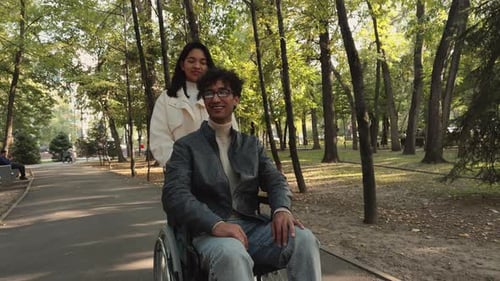 Young Woman Pushing Her Boyfriend in a Wheelchair in the Park