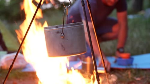 A tripod stands on a campfire where the water boils
