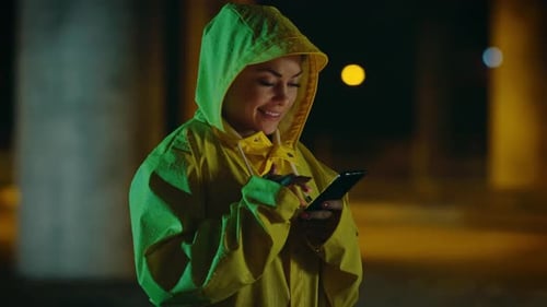 Woman in Yellow Raincoat Uses Smartphone at Night