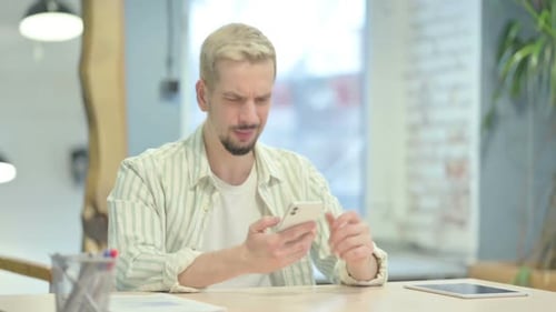 Frustrated Man Using Smartphone at His Desk