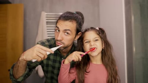 Portrait of a Brunette Man in a Green Checkered Shirt Brushing His Teeth with His Little Daughter
