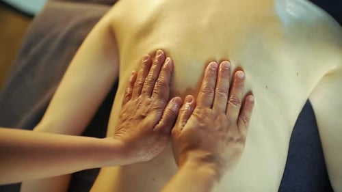 Der Masseur massiert den Rücken des Mädchens mit Massageöl von unten nach oben.