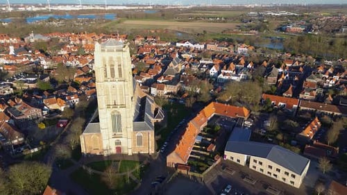 Aerial view of a historic town with a tall Gothic church in the center. Red-roofed houses