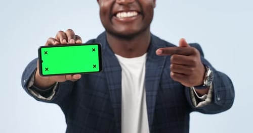 Happy man, phone and pointing to green screen in marketing or advertising against a studio