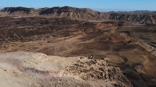 Rotating shot around tourists sitting on the edge of the Makhtesh Ramon Crater In Negev Desert, Isra