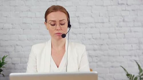Tracking shot of a businesswoman working in customer support at a desk. The woman is working on a la