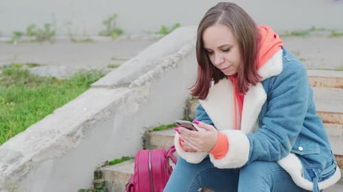 Young Woman with Mobile Phone Sitting on Steps on Street
