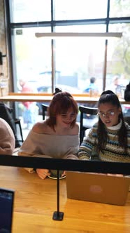 Young Female Friends Working Together with Laptop Computer at Outdoor Cafe