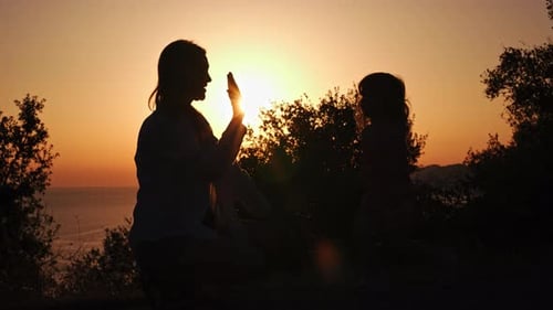 Little Girl Child Give High Five to Her Mother Against Backdrop of Sunset in Park