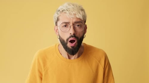 Man looking at camera with big eyes, says wow, isolated on yellow background in studio