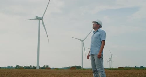 Windmill Engineer in a Hard Hat Inspects the Work Done While Standing Field