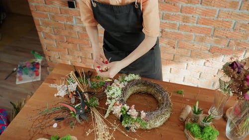 Woman crafting floral wreath at a rustic table