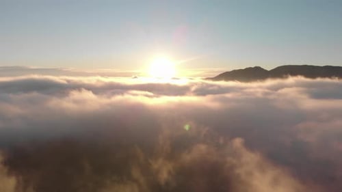 Aerial descent into foggy valley sunrise, sun over misty sea of cloud
