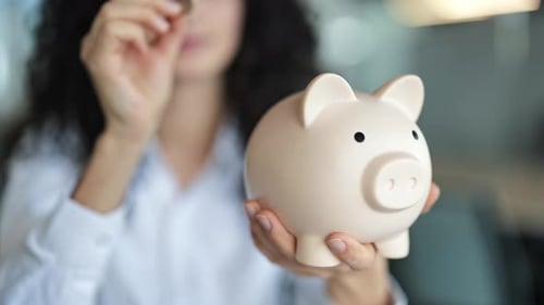 Businesswoman Putting Coin in Piggy Bank Saving Money and Planning Budget at the Office