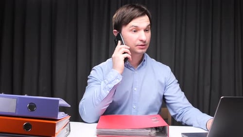 Office Worker Talking on Phone and Working on Laptop at Night