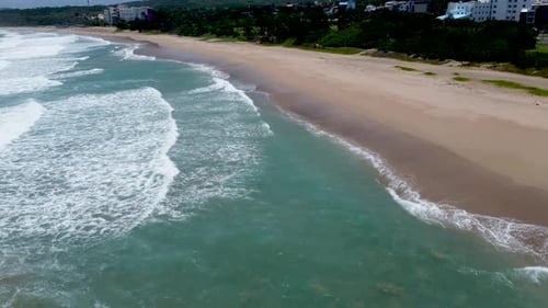 Aerial shot of waves gently breaking on the shore of a secluded beach, lush greenery in the backgrou