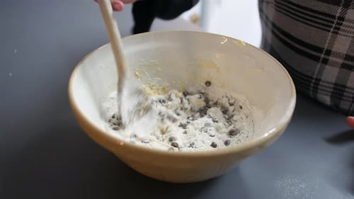 Ein Mädchen mischt in einer Schüssel mit einem Holzlöffel Schokoladenstückchen in die Plätzchenteigkuchenmischung