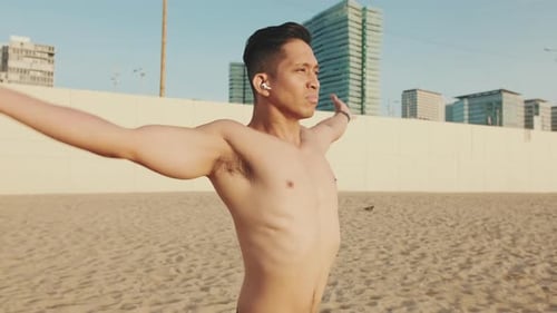 Young athletic man standing on the beach in headphones doing breathing exercises