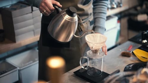 Ein Barista kocht Kaffee in einem Café in Kronstadt, Rumänien. Wasser aus dem Wasserkocher in den F gießen