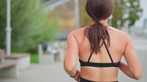 Back View of Lady Running in Black Neck Top with Blurred Trees and Bench Background