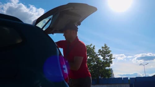 Young Courier Driver in Cap Unloading Cardboard Boxes From Car While Standing Outdoor Parcel