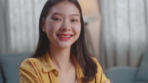 Close Up Of Young Asian Female Smiling To The Camera While Studying By Reading Books At Home