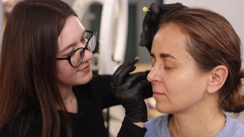 Aesthetician works on woman's eyebrows in salon