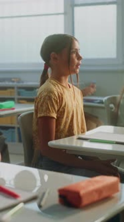 Primary School Children Sitting at the Desks Listening to Lecture Raising Hands to Give Correct