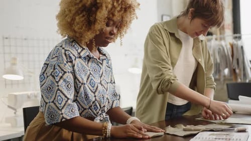 Two Seamstresses Sewing by Hand and Cutting Fabric in Atelier