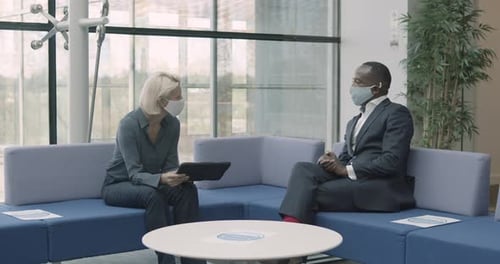Business people in office meeting on sofa wearing face mask with digital tablet in lobby