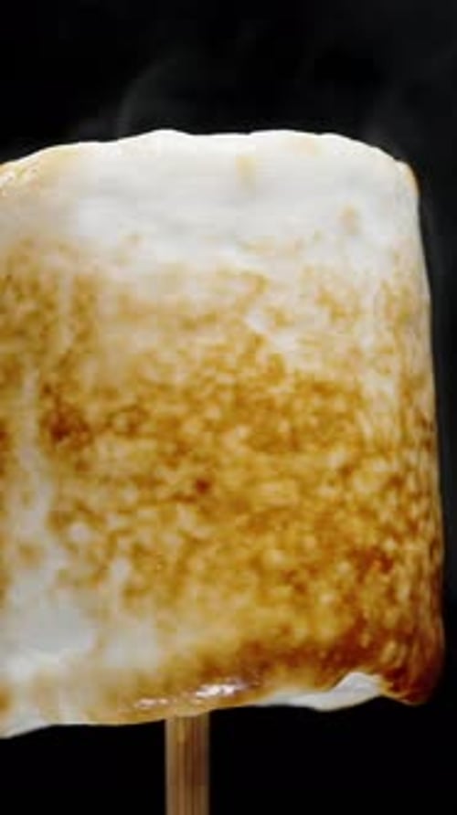 Vertical video. Marshmallow Covered with Sweet Caramel Crust Rotating and Roasting on Fire, Isolated