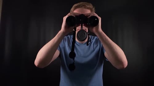 Auburn-haired man looking through binoculars indoors