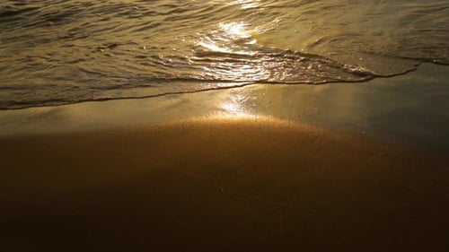 Friedliche Wellen, die während des Sonnenuntergangs über glatten, nassen Sand rollen - Nahaufnahme