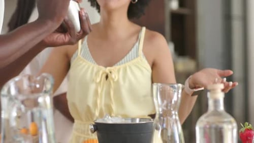 African American couple preparing drinks at kitchen counter, man entering with metal shaker shaking