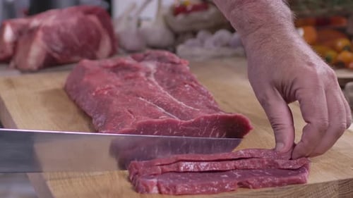 Man Cuts Raw Meat into Strips on Cutting Board