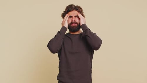 Man Experiencing Headache Massaging Temples in Studio Setting