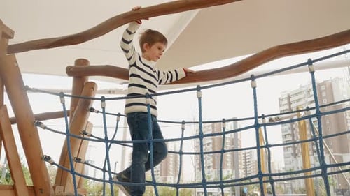 Little boy balancing on the wooden rope bridge at outdoor playground in park.