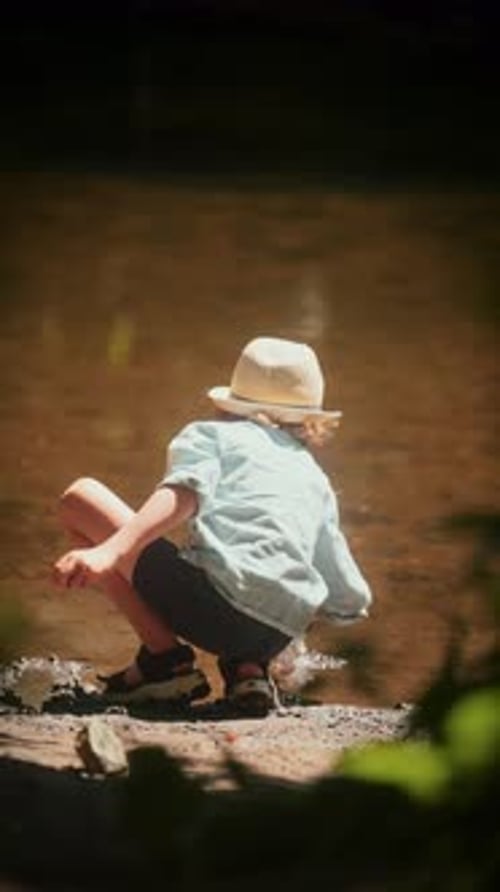 Back View Of Young Boy Playfully Tapping Water In The Creek
