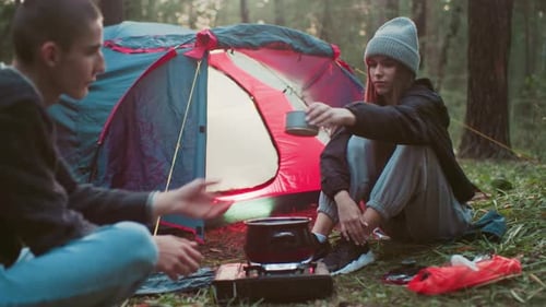 Couple Camping in Forest As Woman Hands Over Canned Food Near Boiling Pot