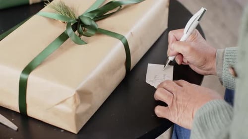 Elderly hands wrapping Christmas gift with green ribbon at home
