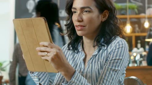 Beautiful Hispanic Woman Uses Tablet Computer while Sitting in the Stylish Cafe.