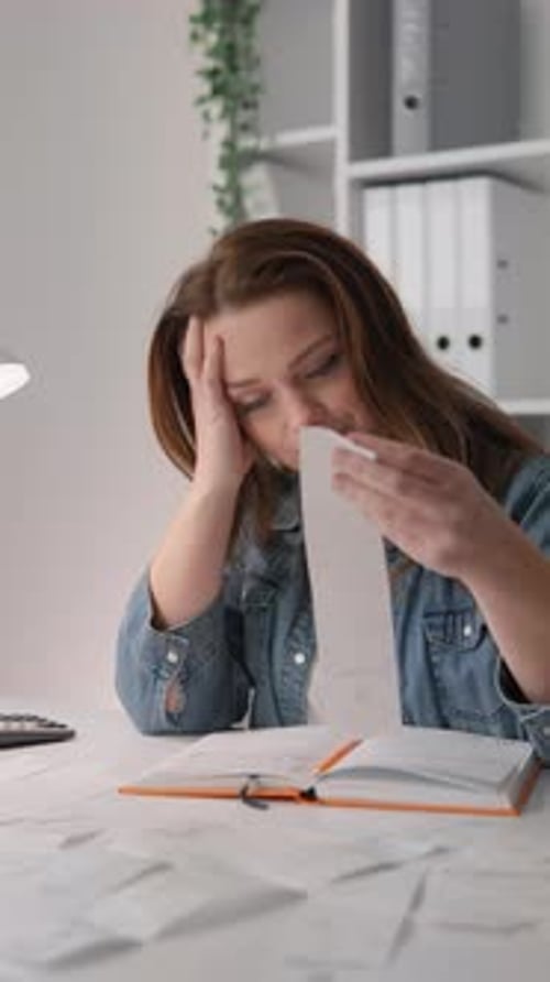 A Stressed Young Woman is Overwhelmed By Accounting and Financial Paperwork While Reviewing Bills