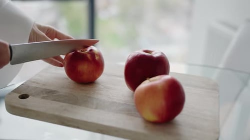 Person Slicing Red Apples on Wooden Cutting Board in Bright Kitchen