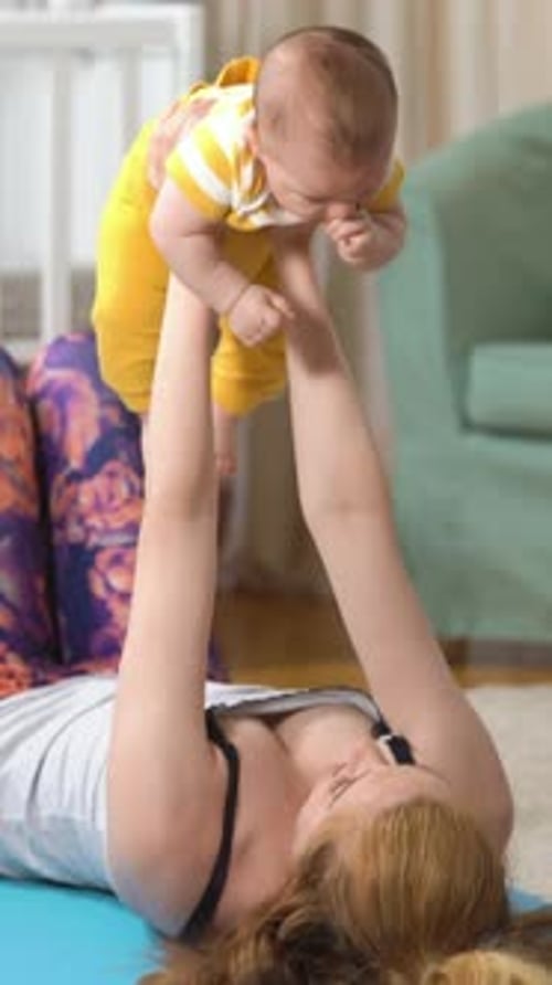 Woman holding baby up above her while lying down