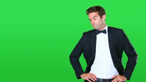 Vídeo de alta definição de um jovem bonito em um smoking parecendo impaciente contra uma tela verde