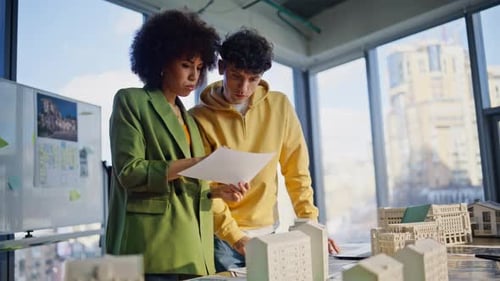 Two Architects Reading Buildings Documents Working on Town Area Layout in Office