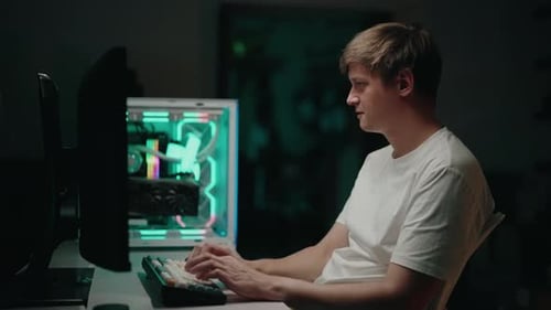 Stressed Programmer Male Working Intently on Desktop Computer Mechanical Keyboard Glowing in Dimly